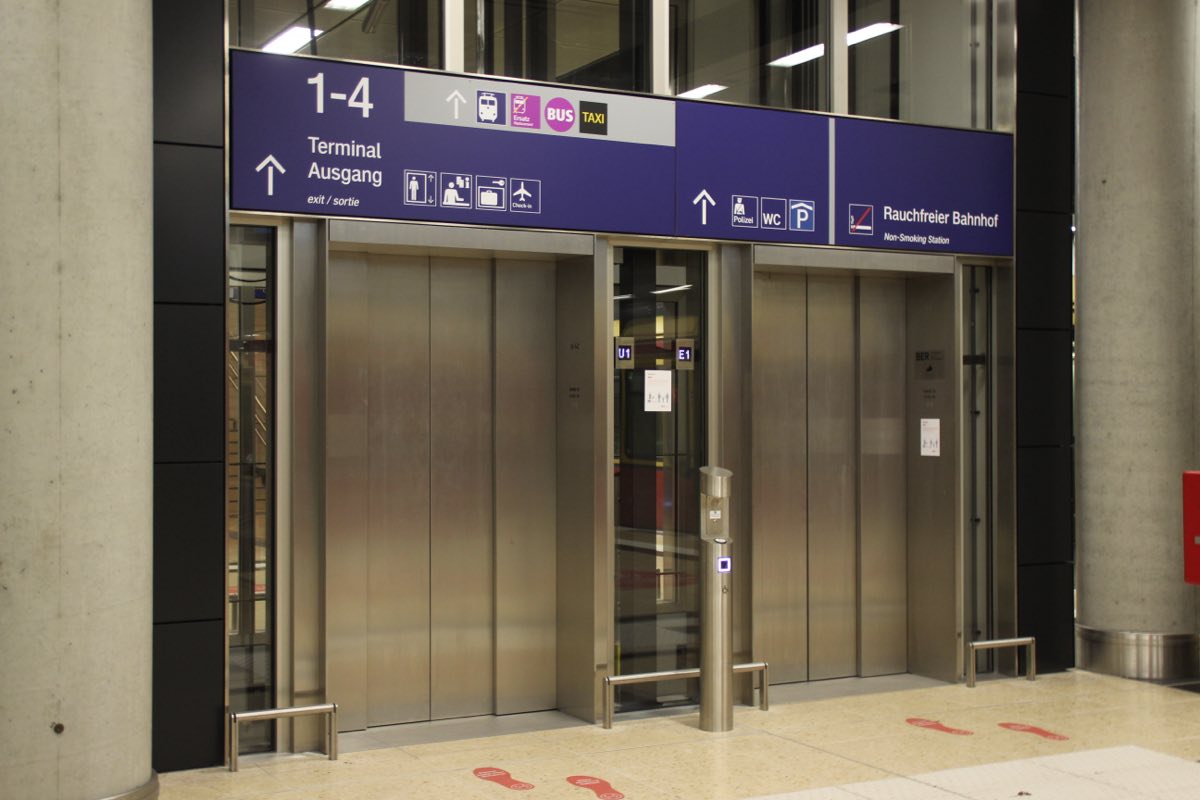 Zwei Aufzüge auf dem S-Bahnsteig im Bahnhof Flughafen BER, darüber die Beschilderung zu Terminal und Ausgang