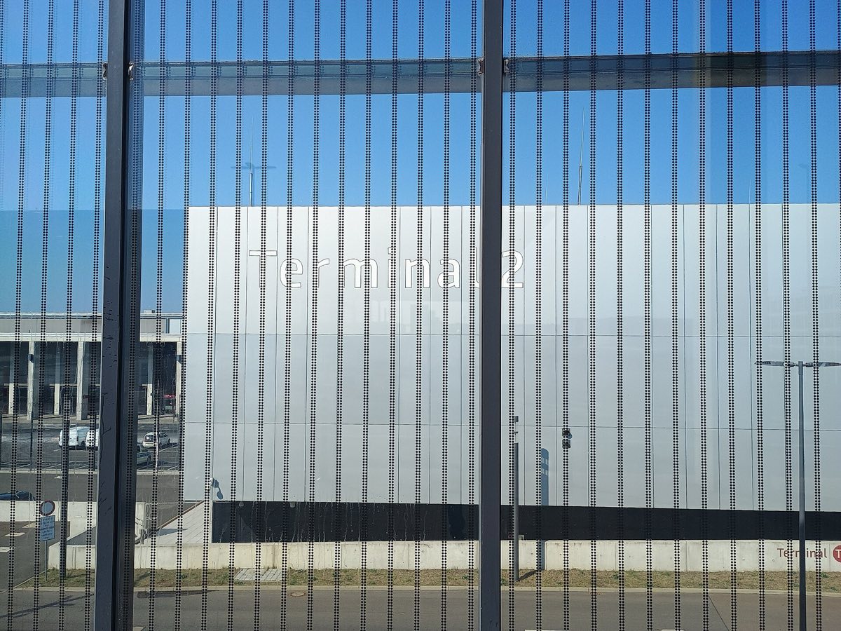 Fassade des Terminal 2 am Flughafen BER mit Schriftzug, gesehen durch die Glasfront des Terminal 1